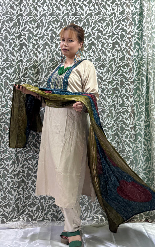 🔹 Color Combination:
	•	Kurta & Pants: Soft Ivory/Cream
	•	Neck Embroidery: Deep Blue & Metallic Gold accents
	•	Dupatta: Rich mix of Teal Blue, Maroon, and Olive Green with traditional Bandhani print and gold zari borders
